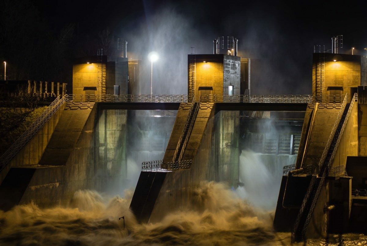 Floodlit dam spillway gates discharging at night.